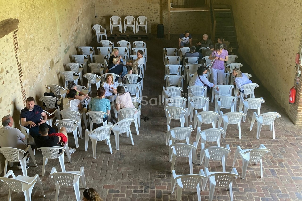 Des groupes de personnes discutent assises sur des chaises blanches dans une grande salle en briques.