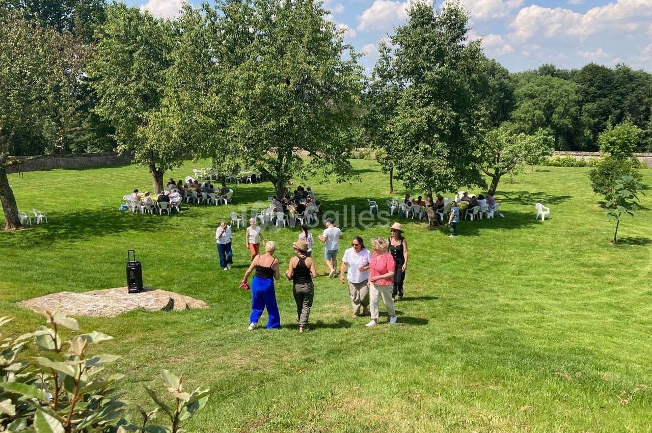 Des personnes se rassemblent dans un parc verdoyant avec des tables et des chaises disposées sous les arbres.