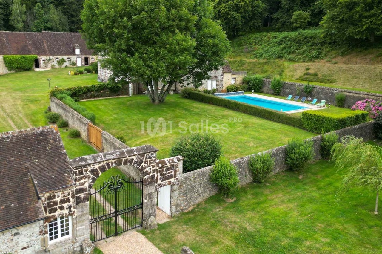 Vue aérienne d'une propriété avec jardin, piscine, bâtiments en pierre et espaces verts entourés de haies.