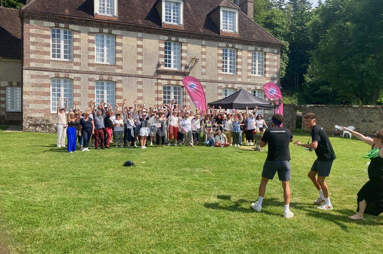 Groupe de personnes rassemblées devant un bâtiment en briques et pierre, sur une pelouse, avec des drapeaux roses.