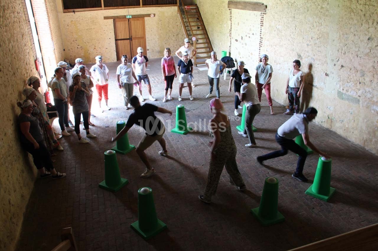 Des personnes participent à une activité ludique en intérieur, disposées autour de cônes verts dans une salle en pierre.