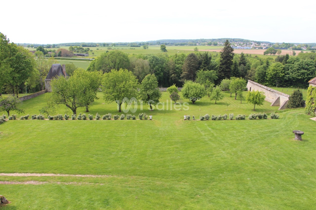 Vue d'un grand jardin verdoyant avec des arbres, des haies et des murs en pierre, entouré d'une campagne vallonnée.