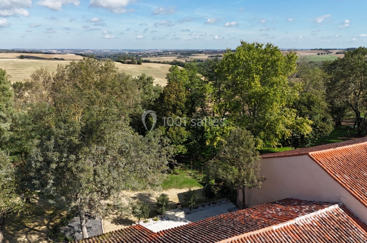 Vue aérienne d'un paysage rural avec des arbres, des champs et une toiture en tuiles rouges au premier plan.