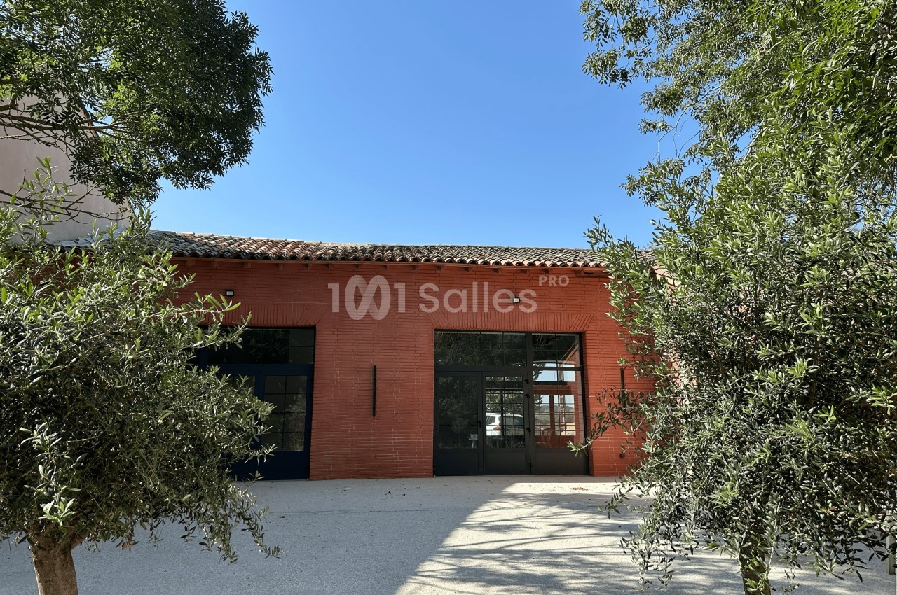 Façade en briques rouges d'un bâtiment avec grandes baies vitrées, entouré d'arbres sous un ciel bleu.