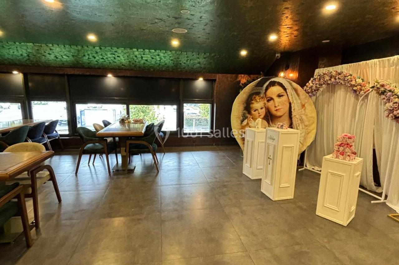 Salle décorée avec des tables, des chaises, une arche florale et une image religieuse en arrière-plan.