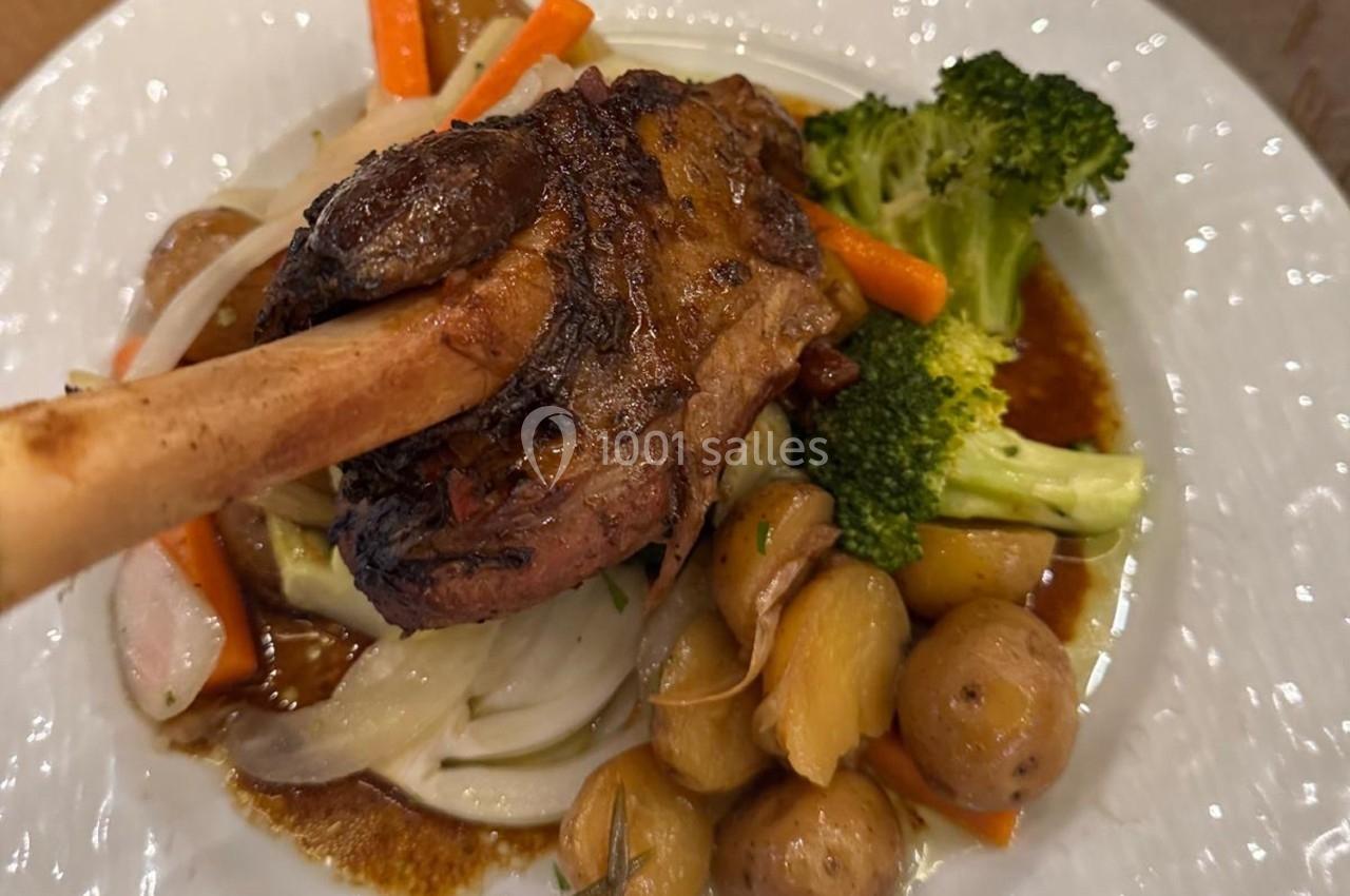 Plat de jarret d'agneau rôti accompagné de légumes variés, pommes de terre, carottes et brocolis, servi sur une assiette…