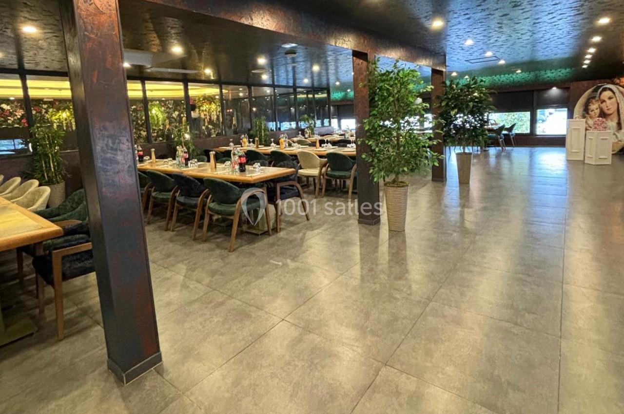 Salle de restaurant spacieuse avec tables dressées, chaises rembourrées et plantes décoratives.