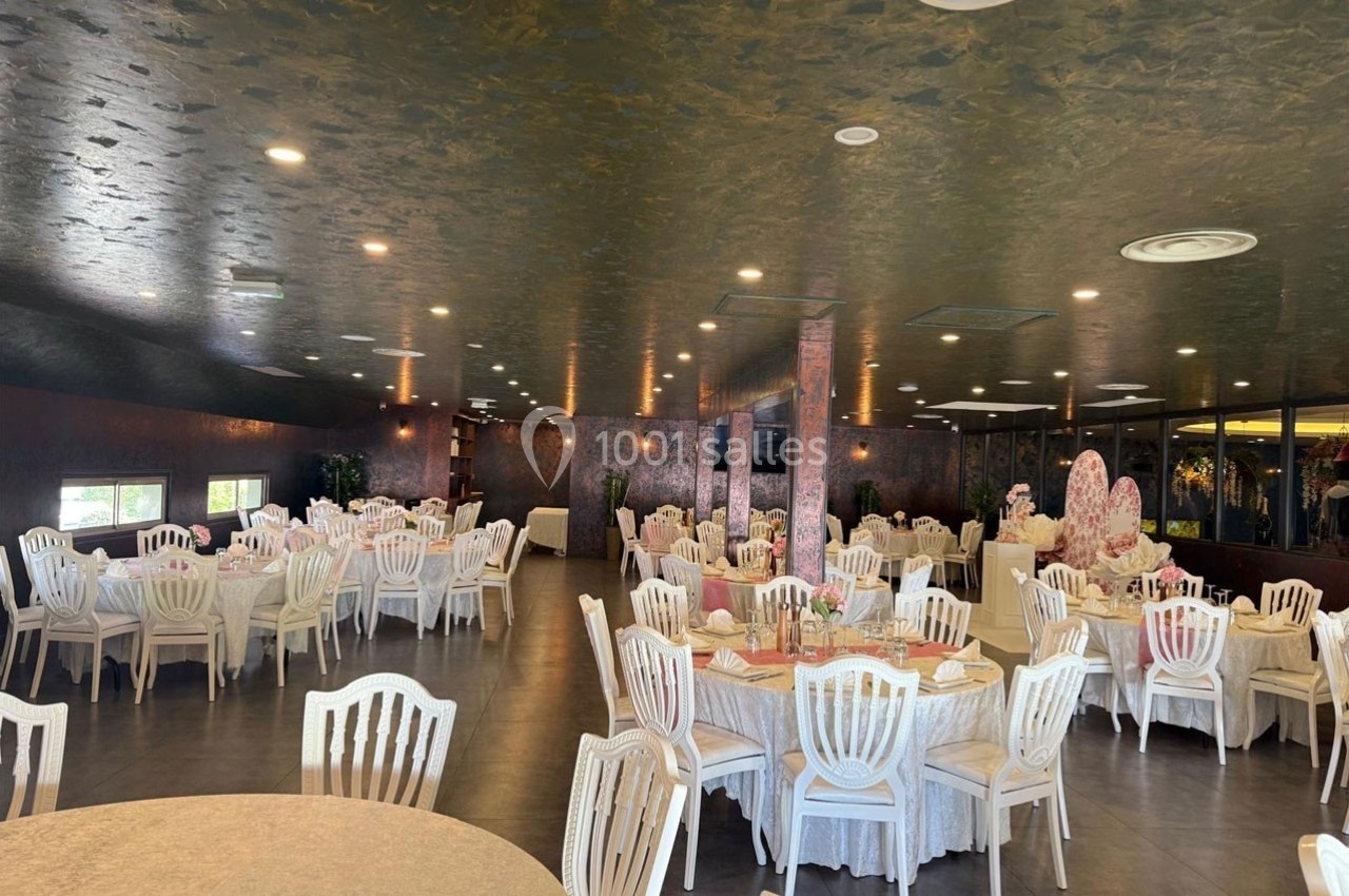 Salle de réception élégante avec tables rondes dressées, chaises blanches et décoration raffinée.