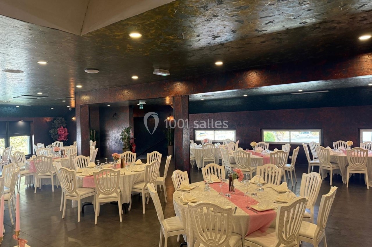 Salle de réception avec tables rondes dressées, nappes blanches, chaises en plastique et décor sobre.