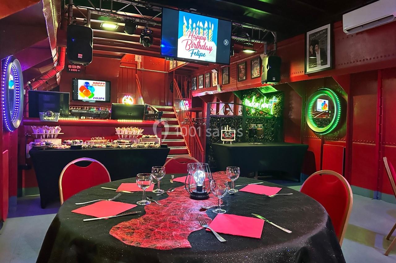 Salle décorée pour une fête d'anniversaire avec table dressée, éclairages colorés et écran affichant un message festif.