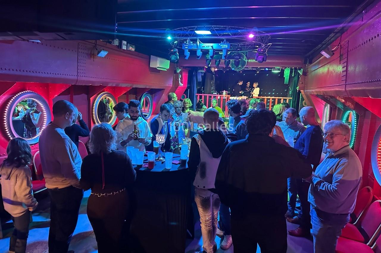 Groupe de personnes discutant autour d'une table dans une salle colorée avec éclairage tamisé et hublots décoratifs.