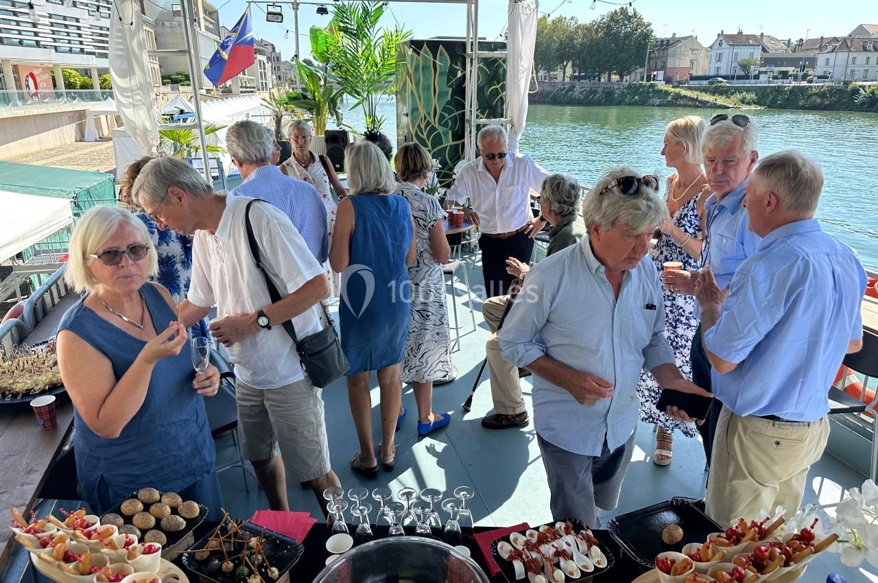 Groupe de personnes discutant et dégustant des amuse-bouches sur une terrasse au bord d'une rivière.