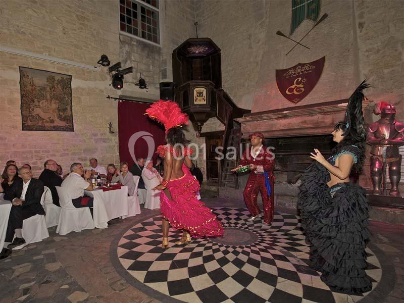 Des danseurs en costumes colorés se produisent devant un public assis dans une salle au décor médiéval.