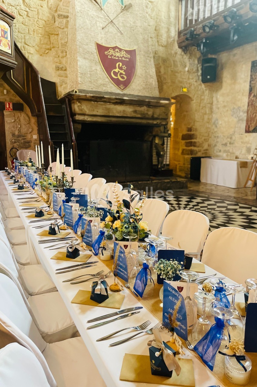 Table de banquet décorée avec des fleurs, des bougies et des cadeaux, dans une salle en pierre au style médiéval.