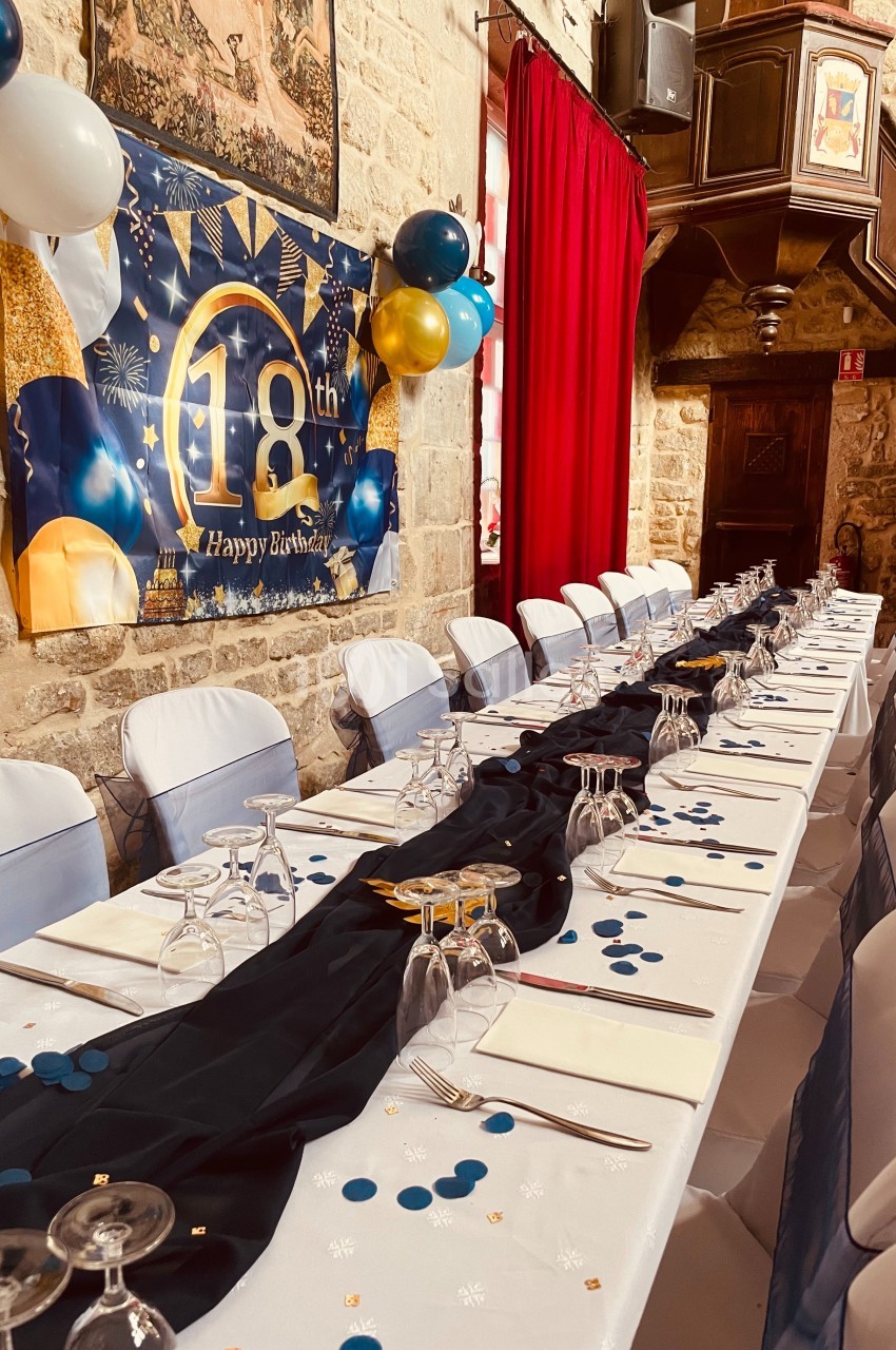 Table décorée pour un 18e anniversaire, avec nappes blanches, chemin de table noir, ballons et bannière festive.