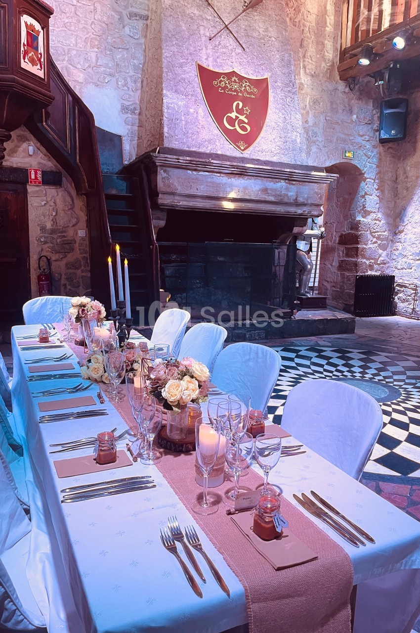 Table de réception élégamment dressée dans une salle en pierre avec cheminée, blason et bougies allumées.