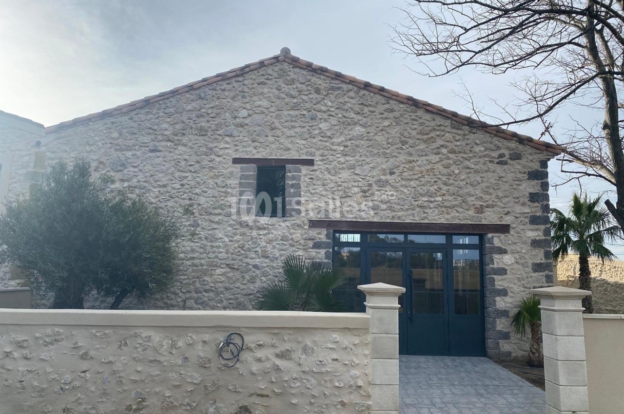 Façade d'une maison en pierre avec toit en tuiles, grande porte vitrée et mur d'enceinte en pierre.
