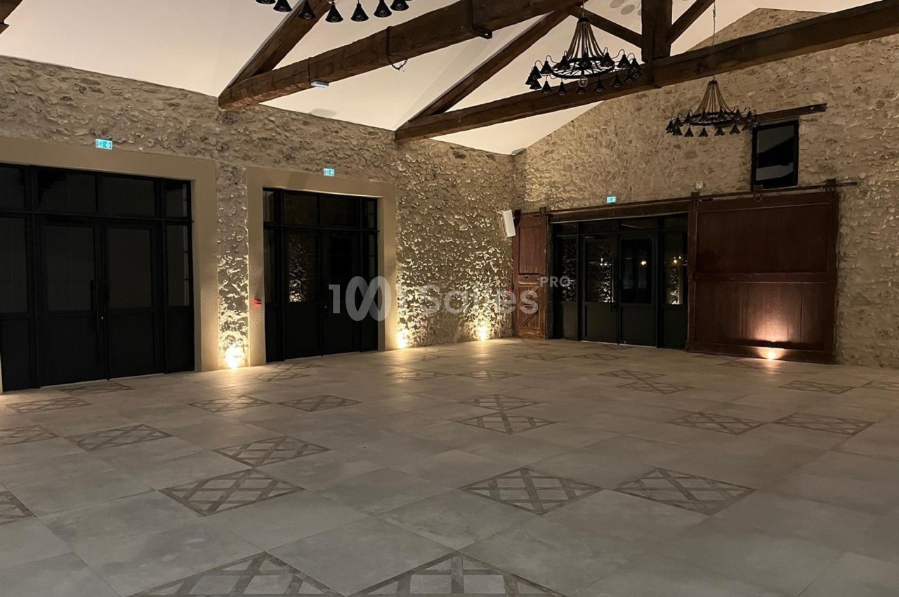 Salle spacieuse avec murs en pierre, poutres apparentes, sol carrelé et éclairage doux.