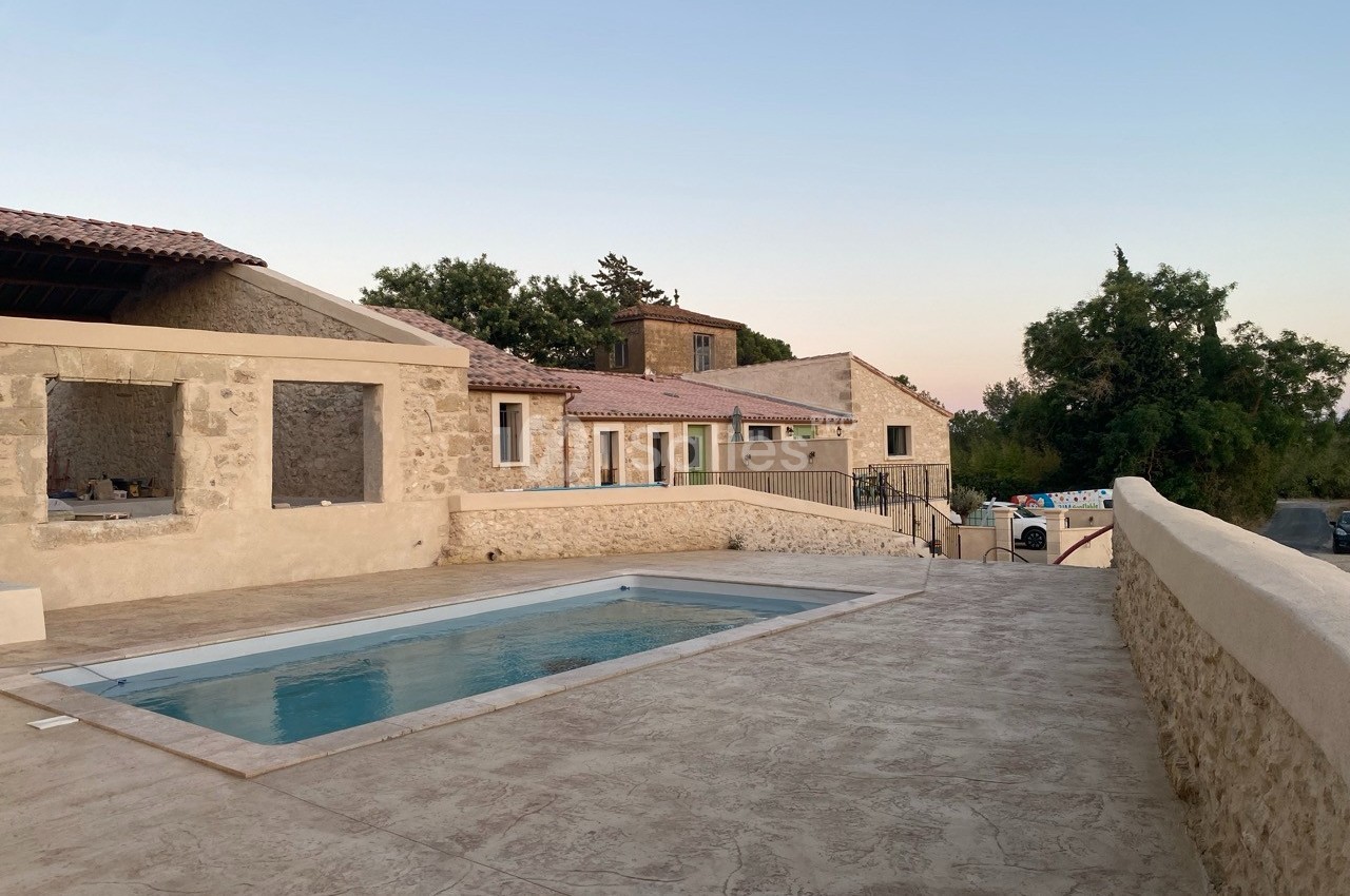 Cour en pierre avec piscine rectangulaire, entourée de bâtiments en pierre et d'arbres sous un ciel dégagé.