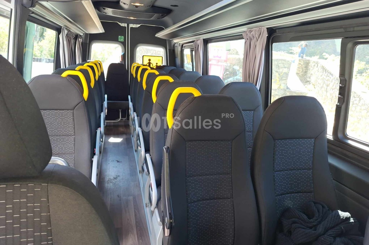 Intérieur d'un minibus avec des sièges noirs et appuie-têtes jaunes, rangés en deux colonnes.