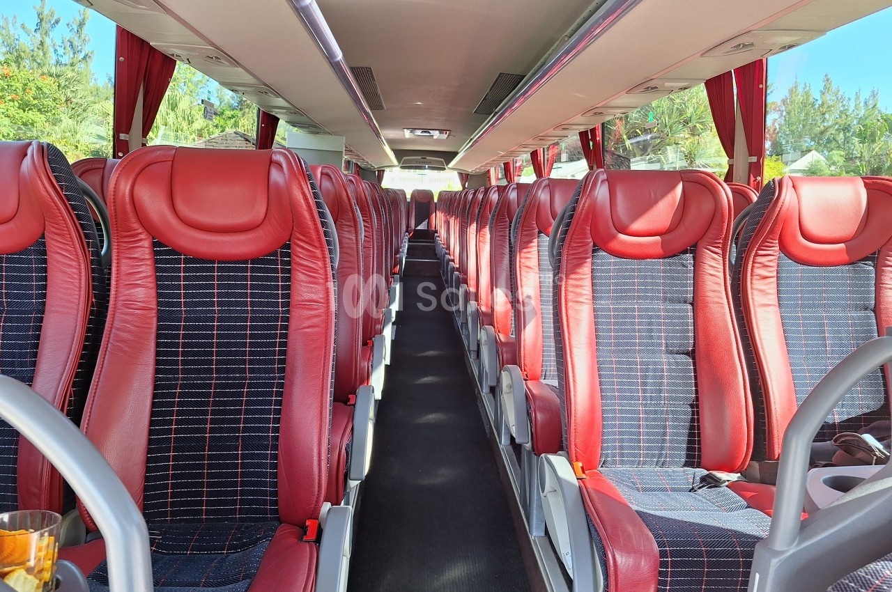 Intérieur d'un autocar avec des sièges rouges et noirs alignés de part et d'autre d'une allée centrale.