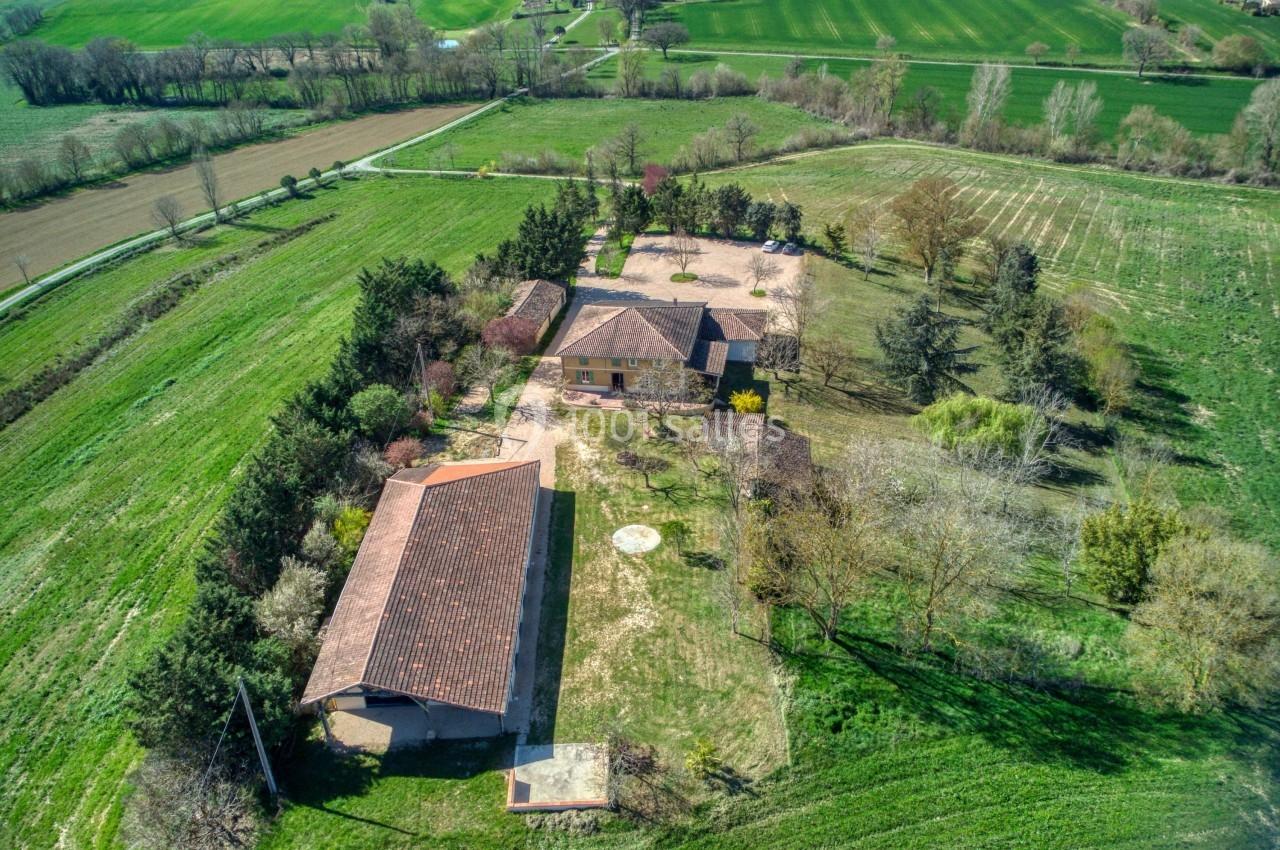 Vue aérienne d'une propriété rurale avec plusieurs bâtiments entourés de champs verts et d'arbres.