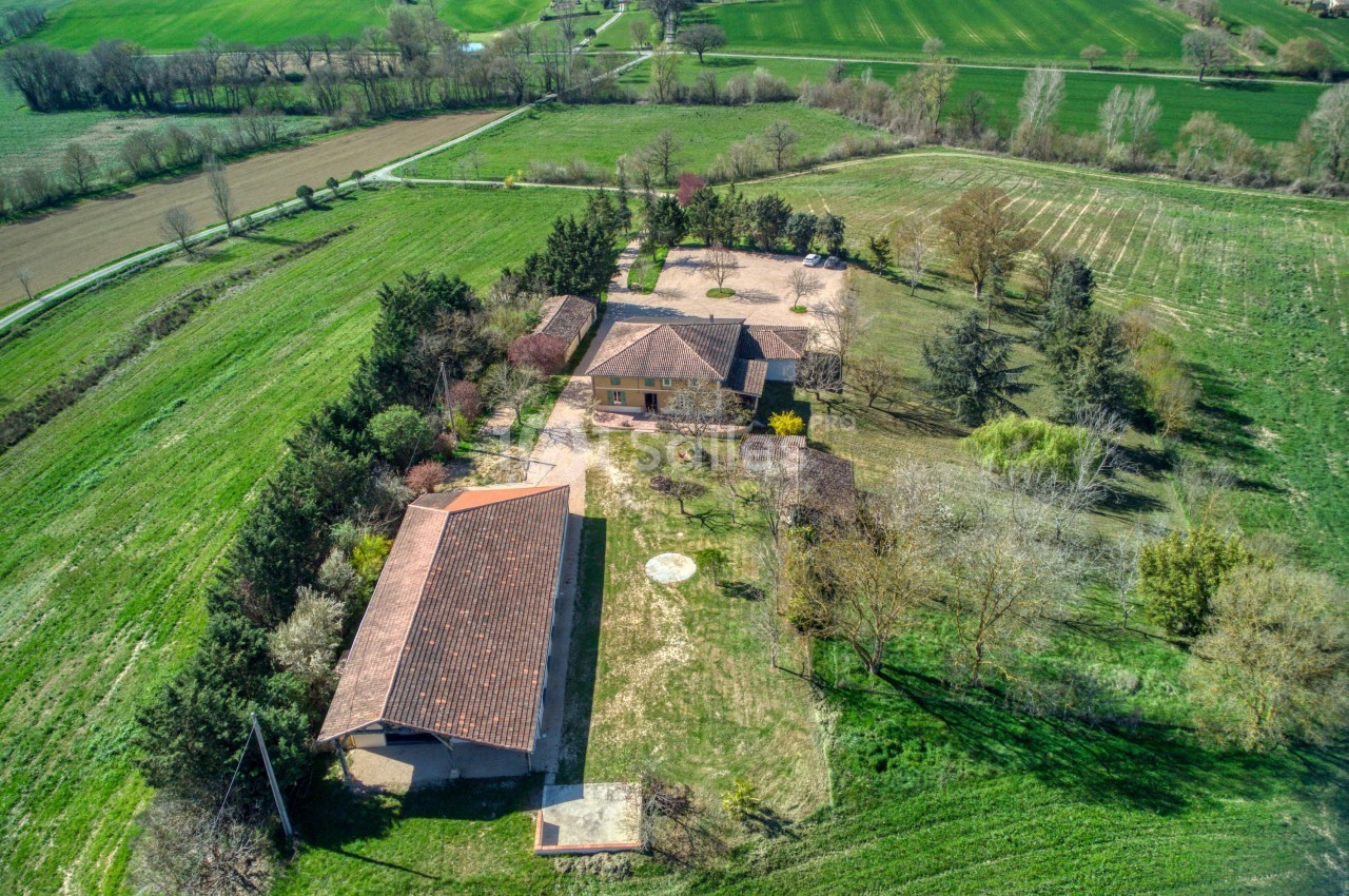 Vue aérienne d'une propriété rurale avec plusieurs bâtiments entourés de champs et d'arbres.