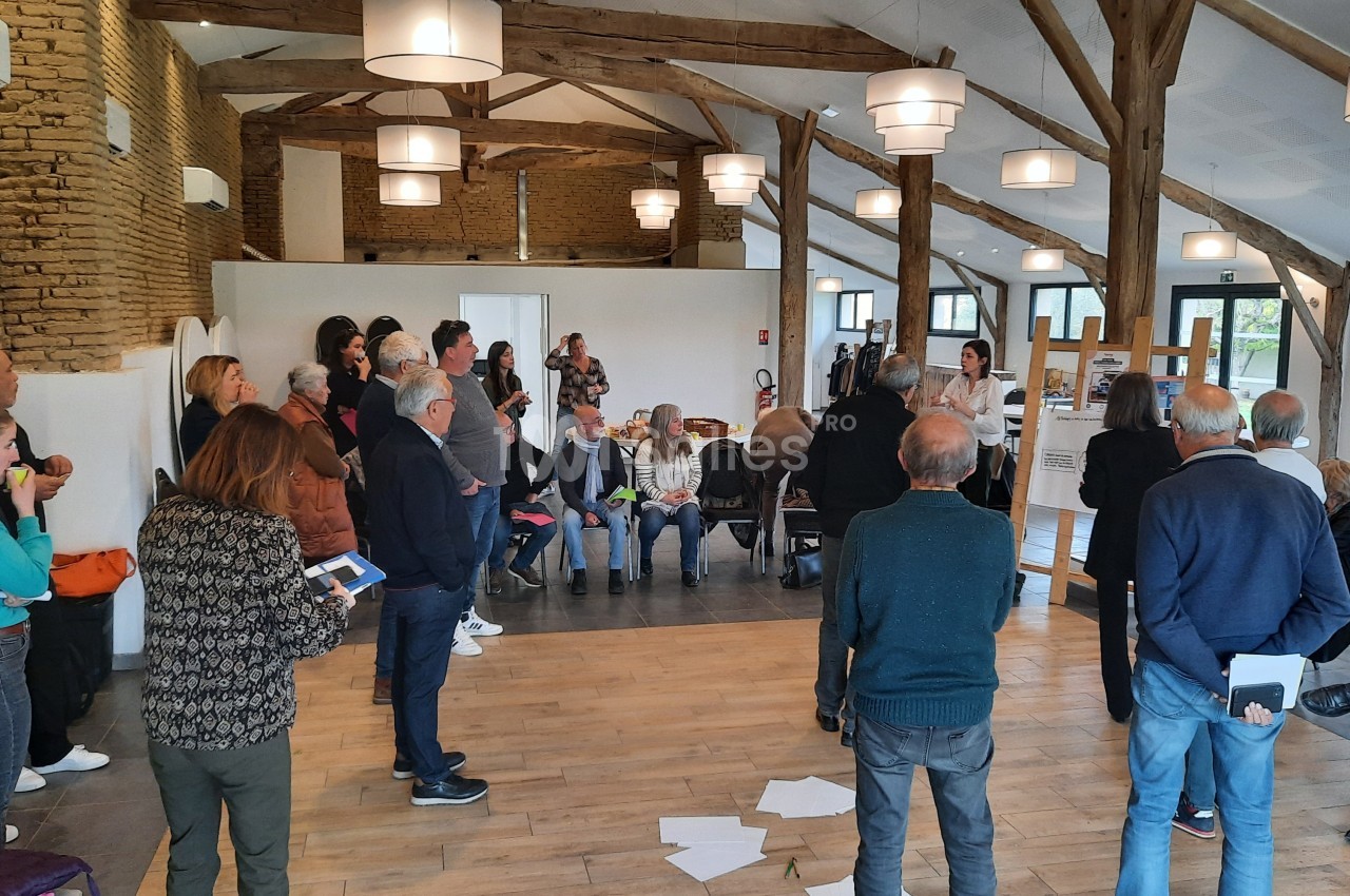 Un groupe de personnes participe à une réunion dans une salle avec des murs en pierre et une charpente apparente.
