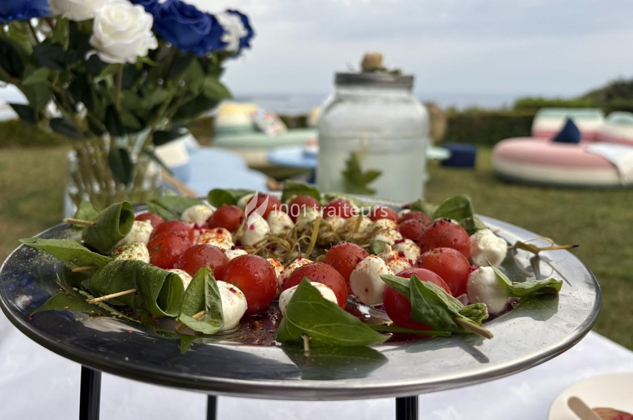Assiette de brochettes de tomates cerises, mozzarella et basilic, présentée sur une table en extérieur.