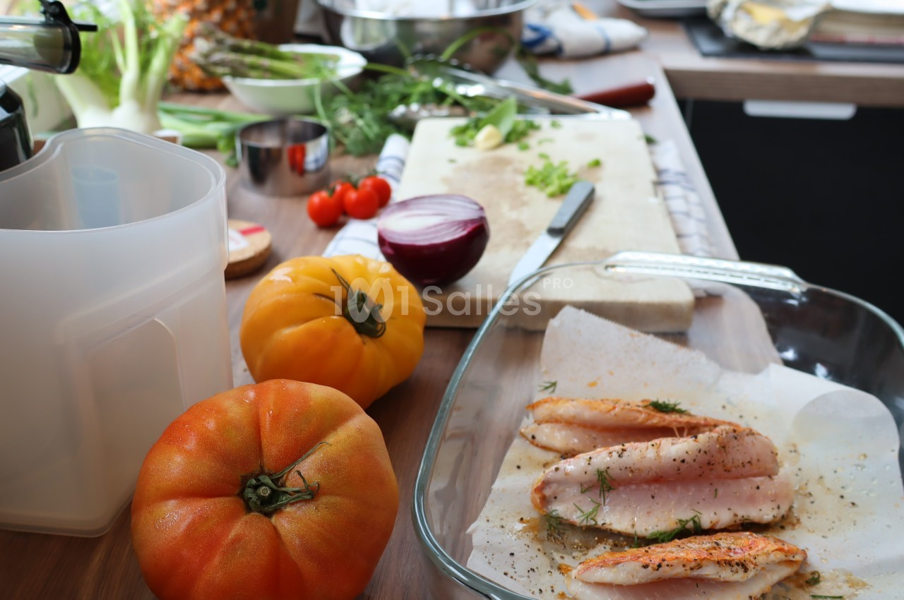 Ingrédients de cuisine sur un plan de travail, incluant tomates, poisson assaisonné et herbes fraîches.