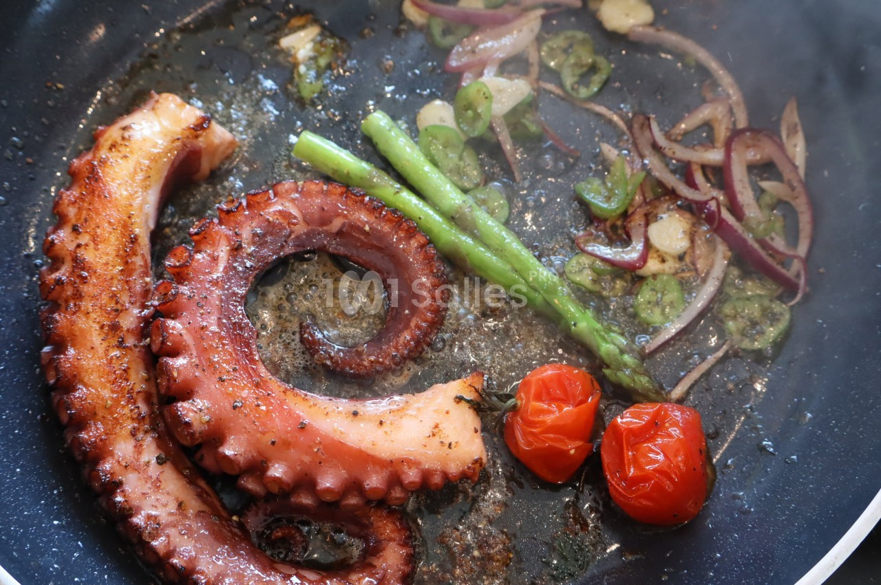 Tentacule de poulpe grillé avec asperges, tomates cerises, oignons et ail dans une poêle.