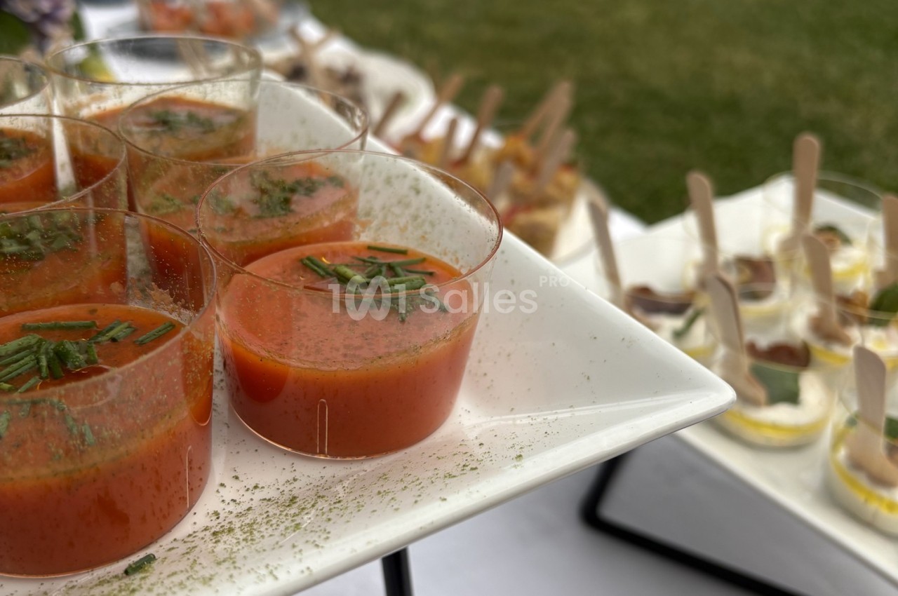 Verrines de soupe rouge garnies de ciboulette, présentées sur un plateau lors d'un buffet en extérieur.