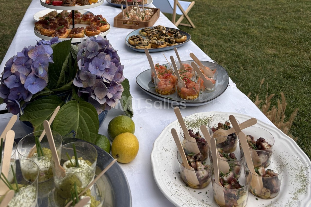 Buffet en plein air avec divers plats et verrines sur une table blanche, décorée d'hortensias et de citrons.