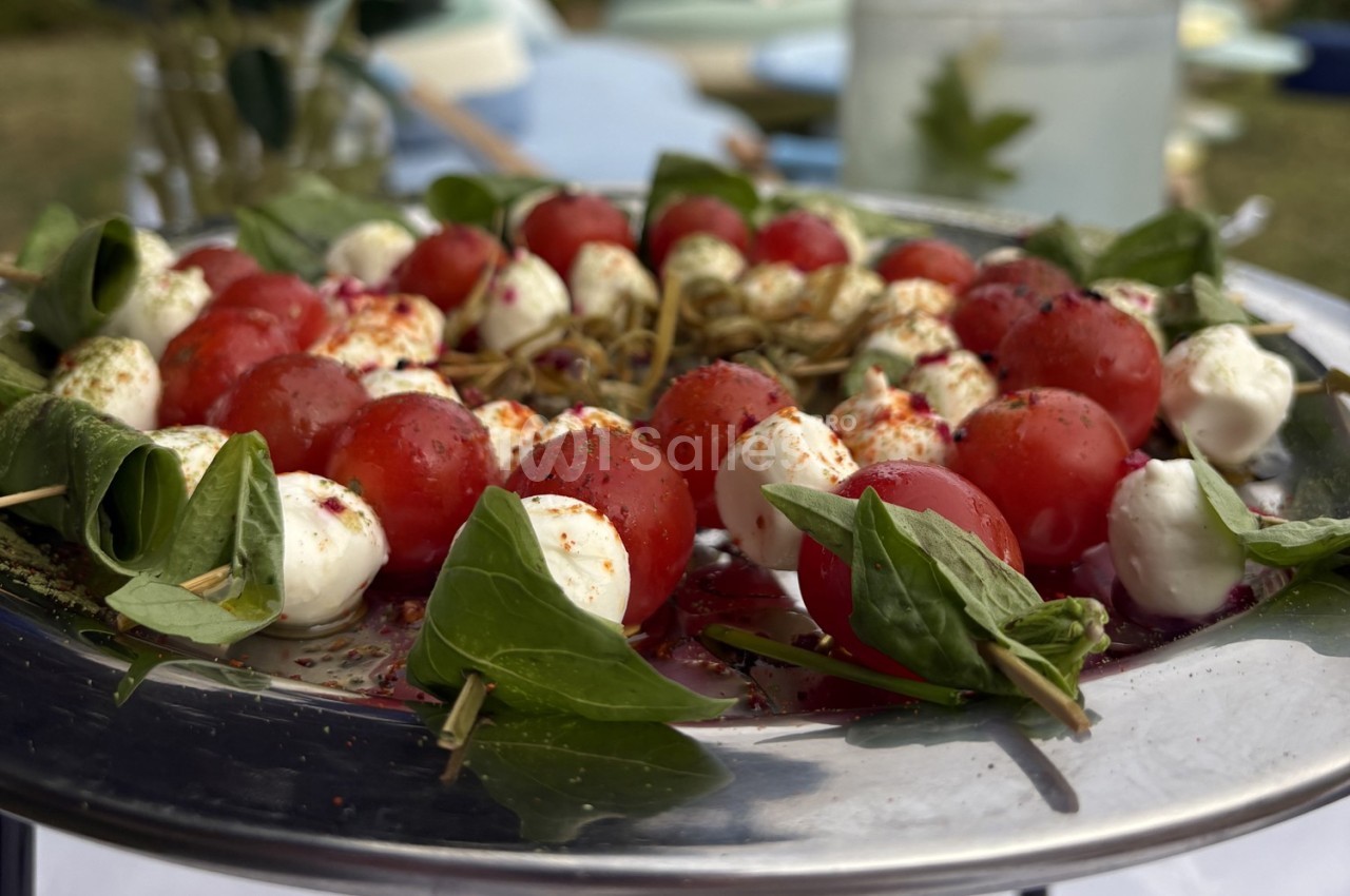 Brochettes de tomates cerises, mozzarella et feuilles de basilic, présentées sur un plateau en métal.