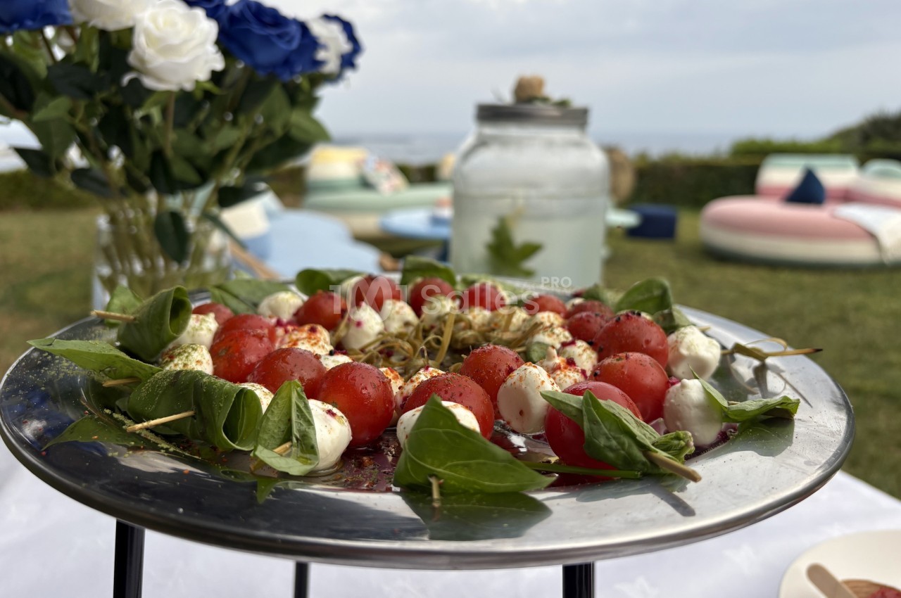 Assiette de brochettes de tomates cerises, mozzarella et basilic, présentée sur une table en extérieur.