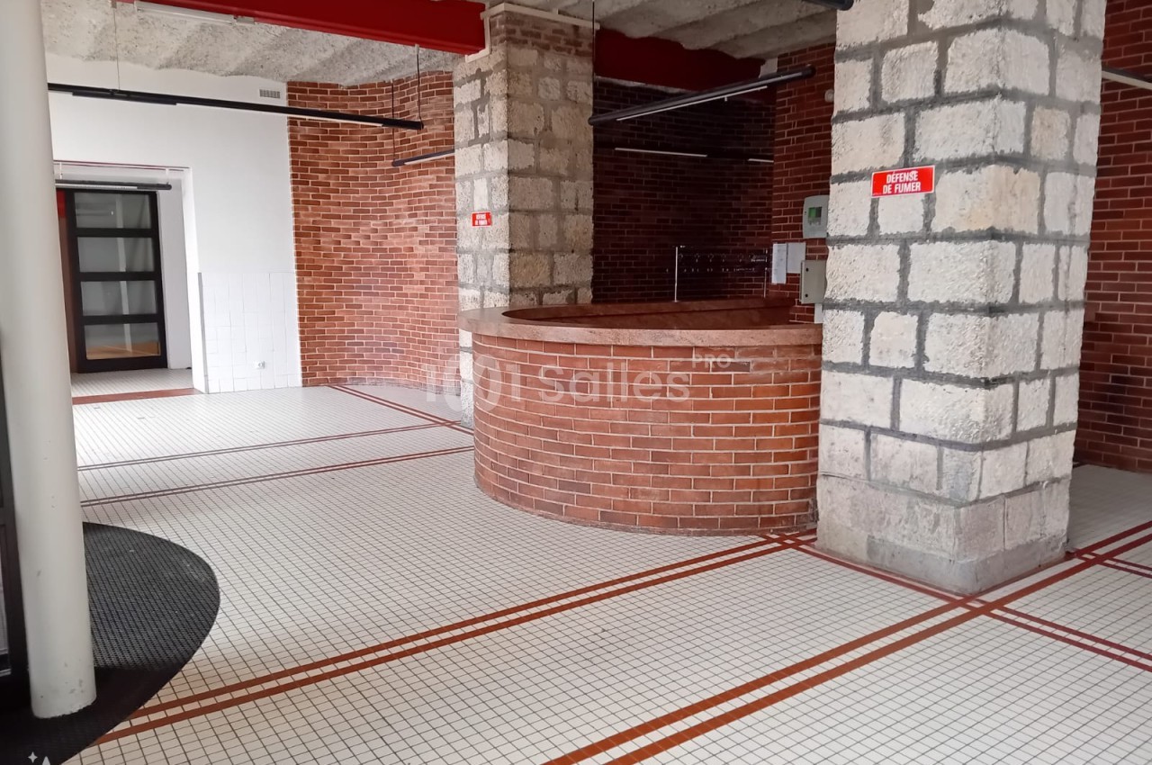 Espace intérieur avec murs en briques et pierres apparentes, sol carrelé blanc à motifs rouges et plafond en béton.