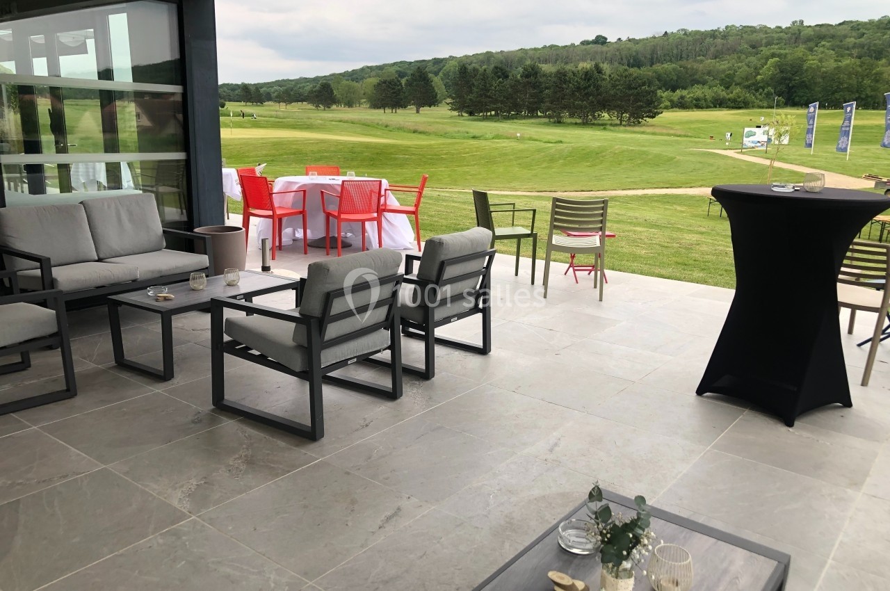 Terrasse aménagée avec mobilier moderne, vue sur un terrain de golf verdoyant sous un ciel nuageux.