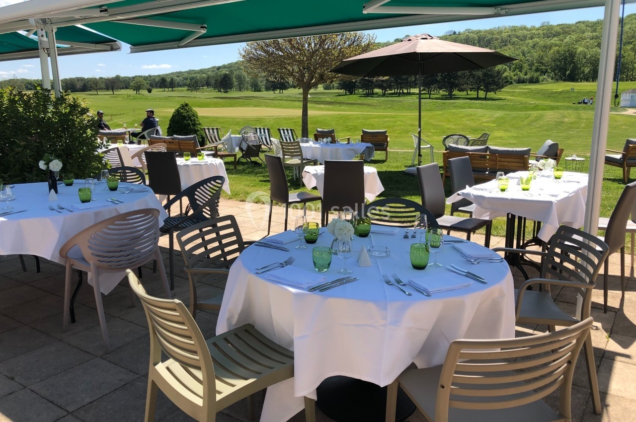 Terrasse d'un restaurant avec tables dressées, vue sur un terrain de golf et un paysage verdoyant en arrière-plan.