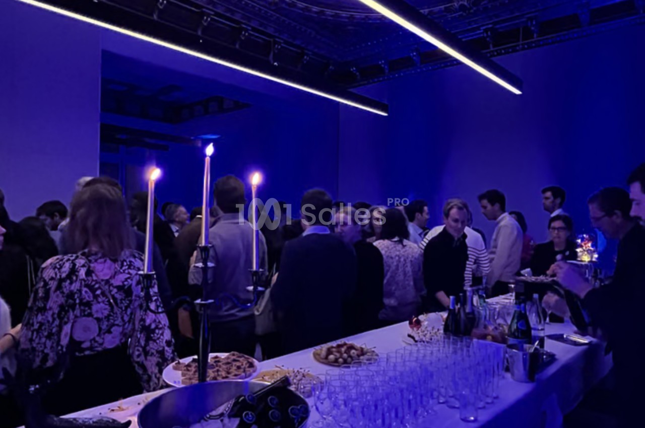 Groupe de personnes rassemblées dans une salle sombre éclairée par des lumières bleues, avec un buffet au premier plan.