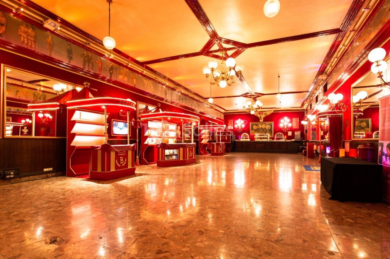 Salle spacieuse au décor rétro avec éclairage chaleureux, murs rouges, vitrines et lustres suspendus.