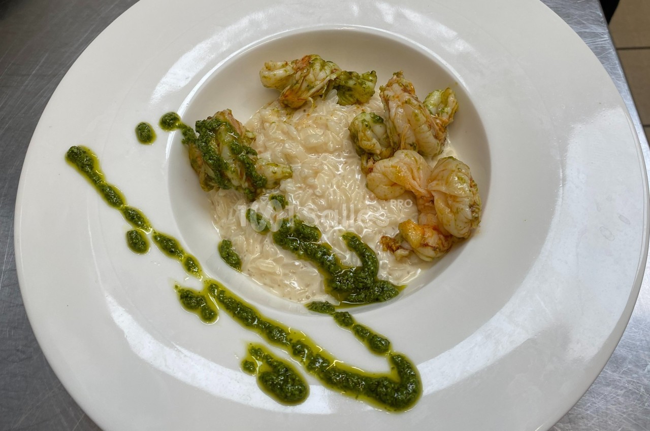 Assiette de risotto crémeux accompagné de crevettes et décorée de sauce verte.