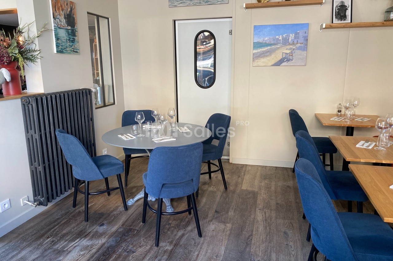 Salle de restaurant avec tables dressées, chaises bleues et décoration murale sobre dans un cadre lumineux.