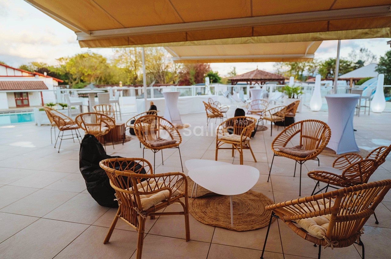 Terrasse aménagée avec des fauteuils en rotin, une table basse blanche et des parasols, près d'une piscine extérieure.