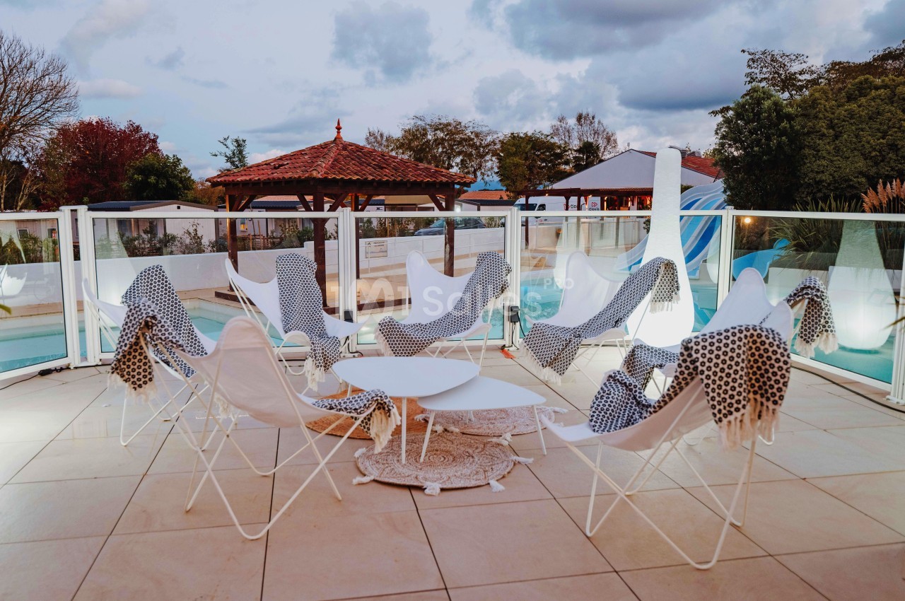 Terrasse avec chaises blanches, plaids à motifs et table basse, près d'une piscine entourée de barrières vitrées.