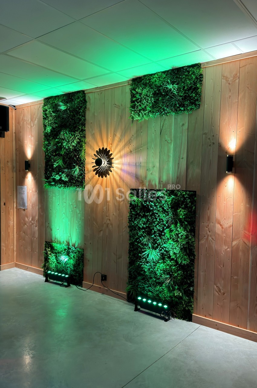 Mur en bois décoré de panneaux végétaux éclairés par des spots verts et des appliques murales.