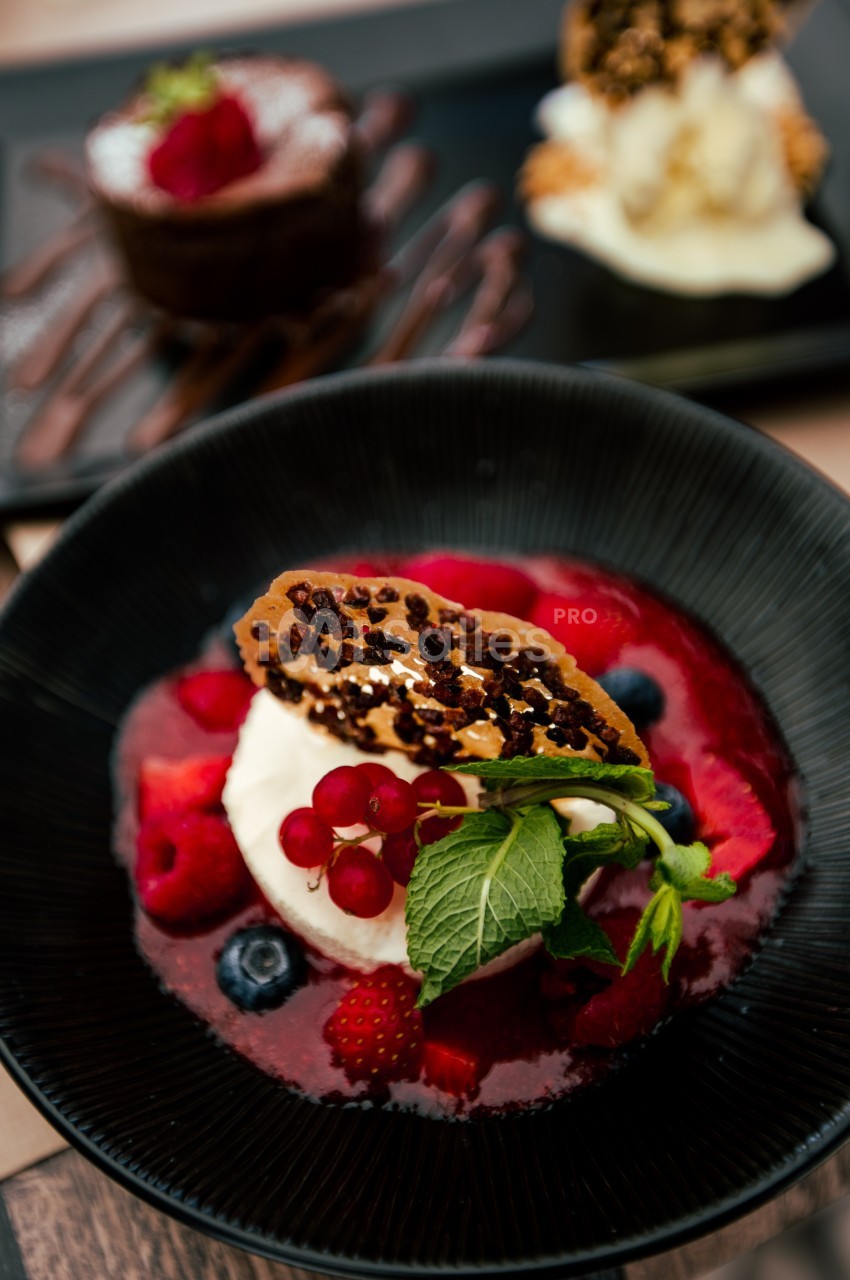Dessert composé de fruits rouges, crème fouettée, tuile croustillante et coulis, présenté dans une assiette noire.
