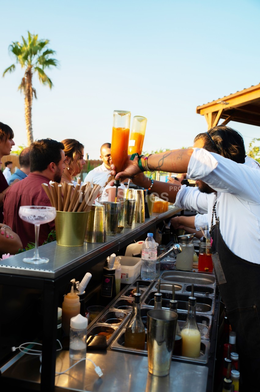 Un barman prépare des cocktails devant un groupe de personnes lors d'un événement en plein air.