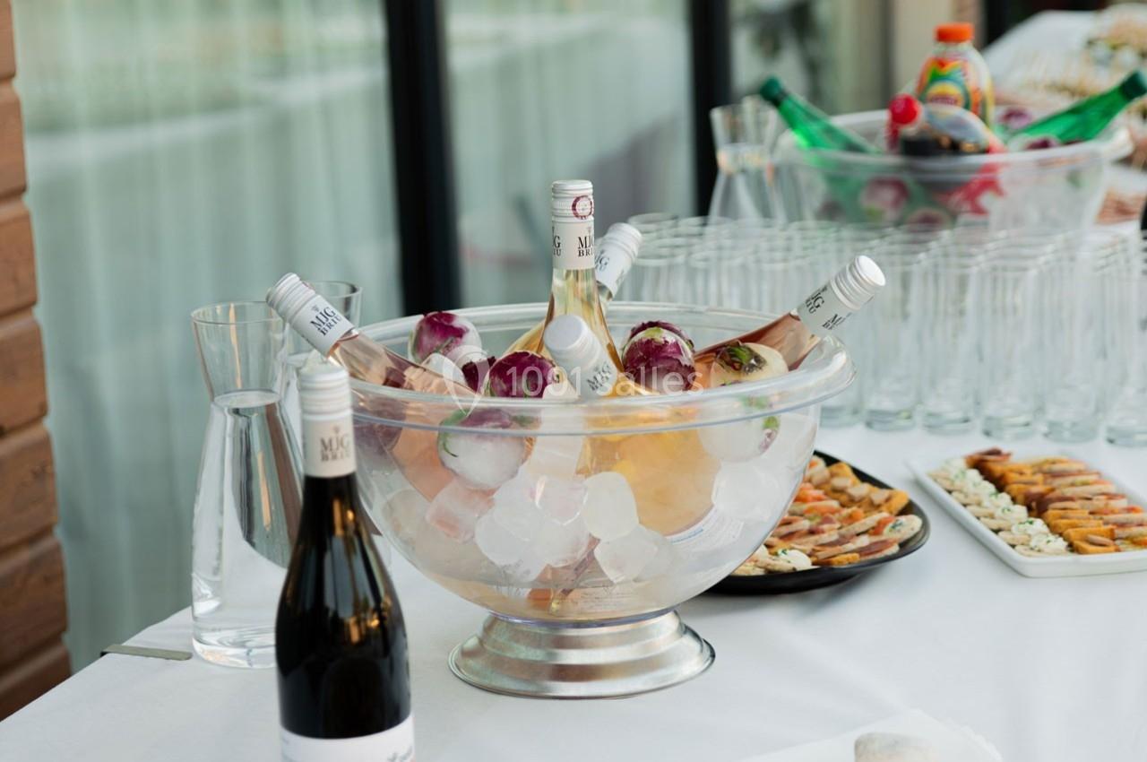 Seau rempli de glace contenant des bouteilles de vin rosé, entouré de verres et d'amuse-bouches sur une table blanche.