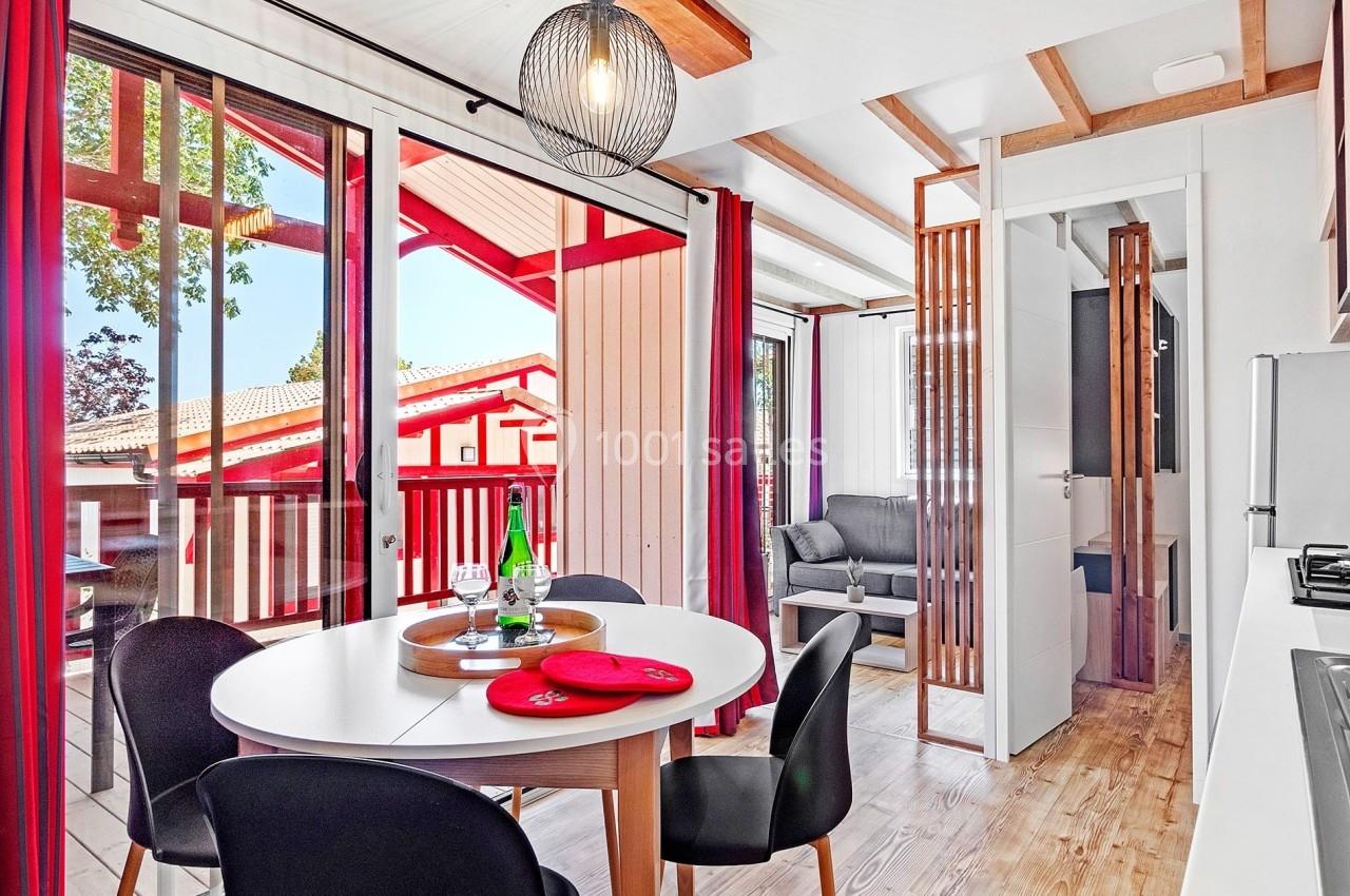 Salle à manger lumineuse avec table ronde, chaises noires, cuisine équipée et vue sur une terrasse en bois.