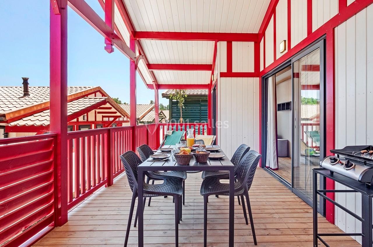 Terrasse en bois avec table dressée, chaises noires, barbecue et vue sur des maisons à colombages rouges et blanches.